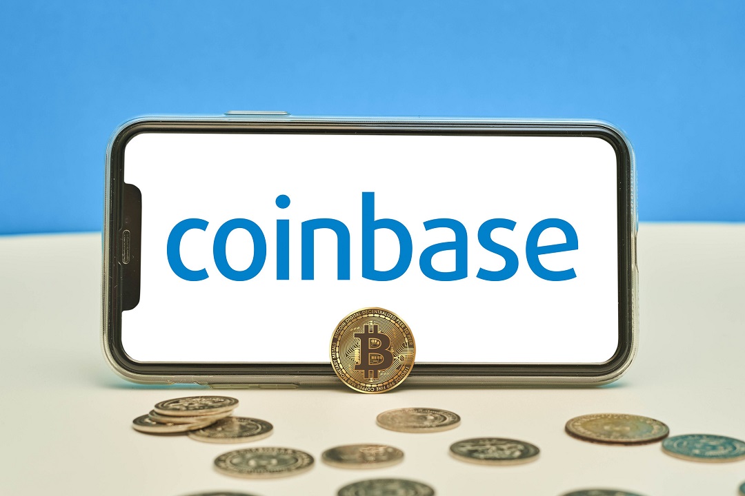 Coinbase logo on a mobile phone with physical bitcoins in front of it